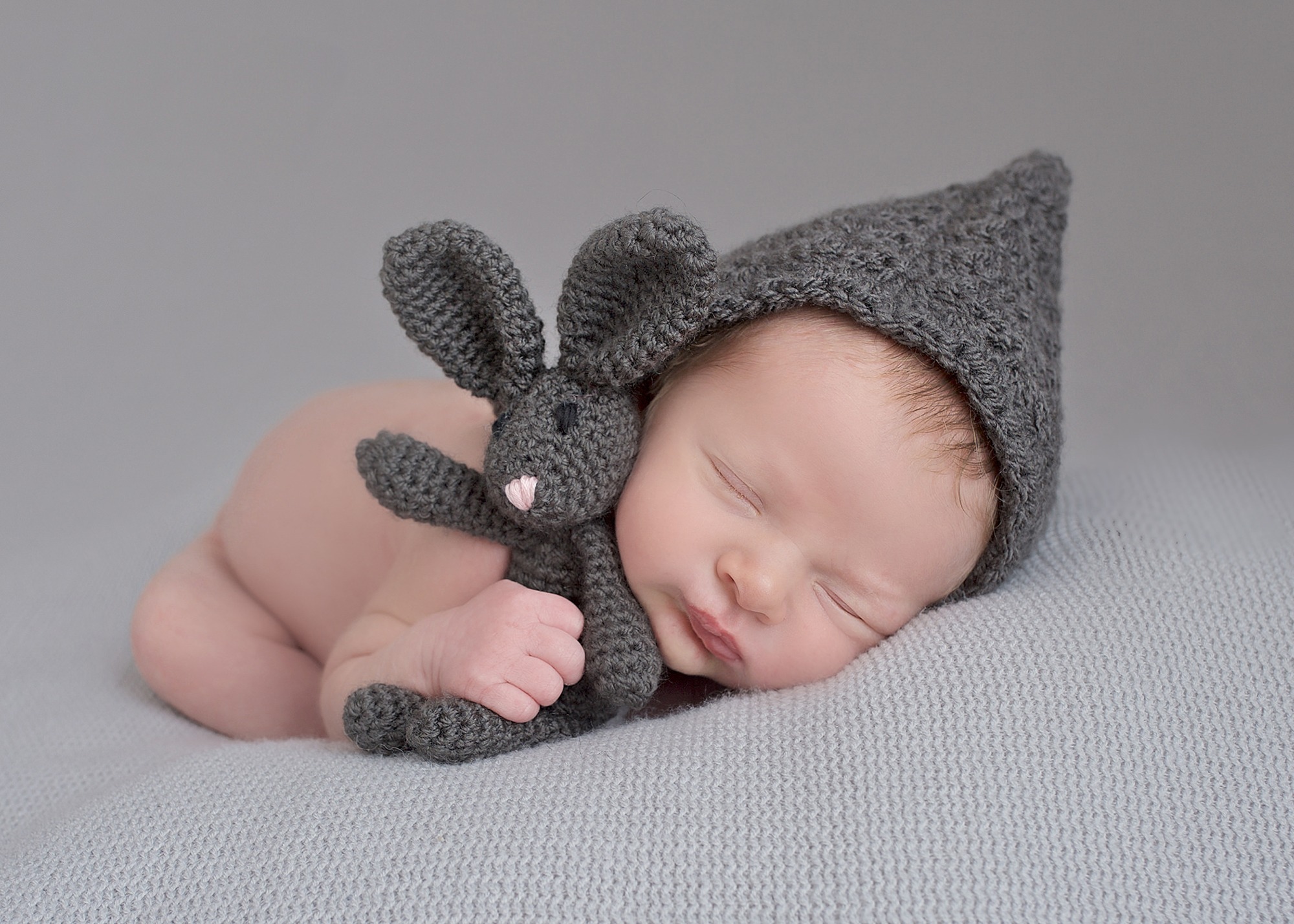 "cute newborn baby holding tiny soft rabbit, with hat on peacefully posed and sleeping"