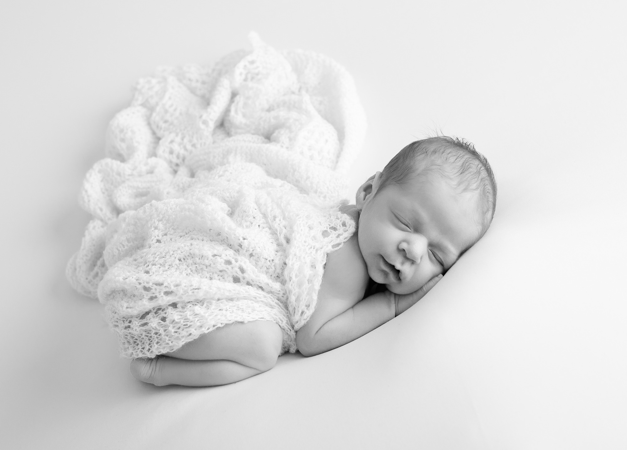 modern image of newborn baby posed asleep on white backdrop material 