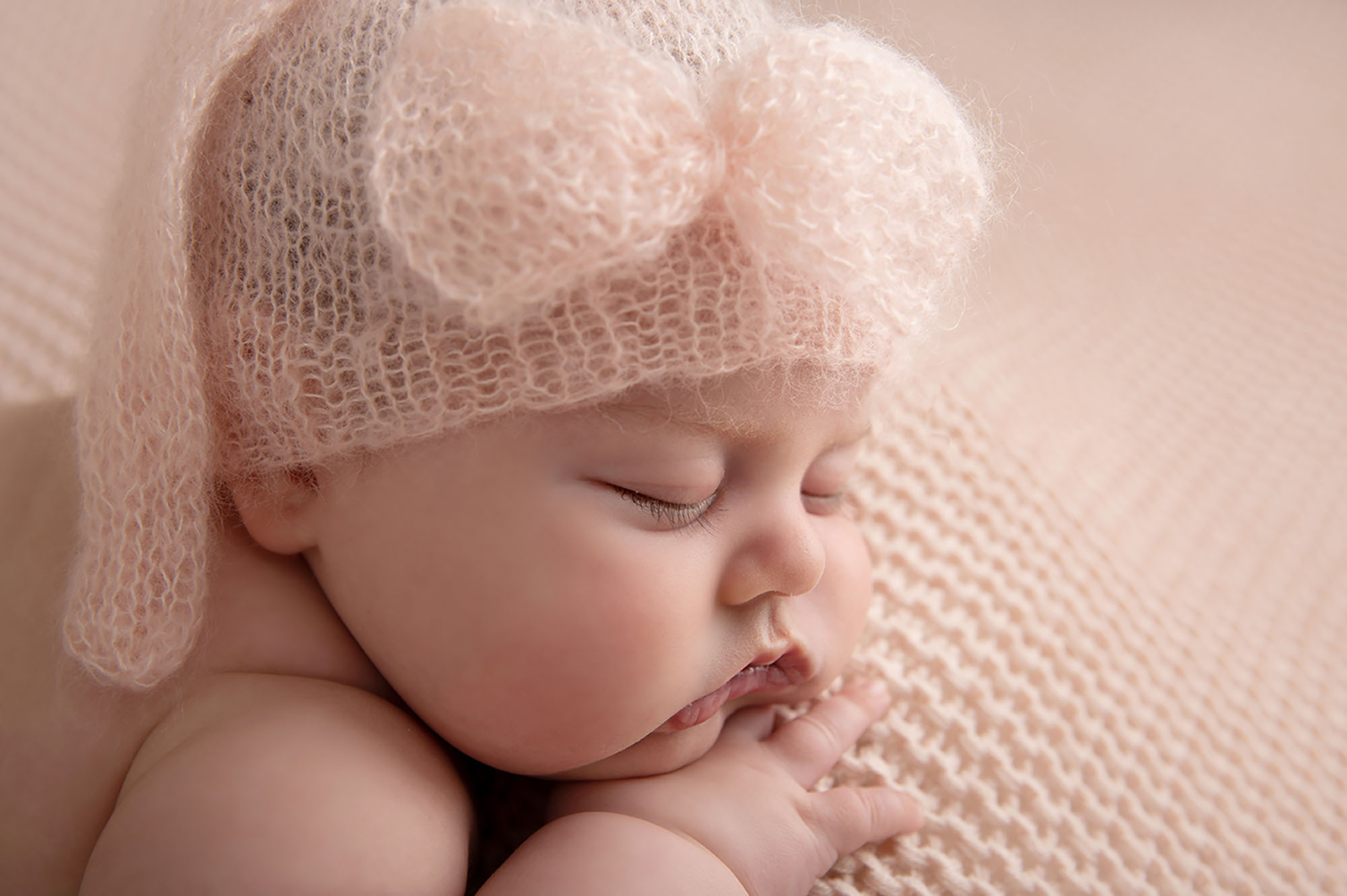 close up portrait of a newborn baby girl wearing pink fluffy hat asleep 