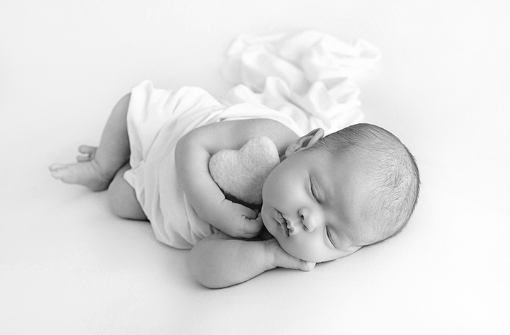 cute newborn baby wrapped in white laying in heart bowl 
